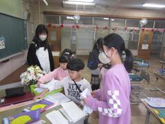 大人と紫の服を着た女の子が見守る中で資料に手を伸ばす2人の子供たちの写真