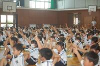 体育館で座り、手を挙げている生徒たちの写真