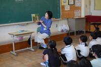 教室で絵本を読んでいる女性と座って話を聞いている生徒たちの写真