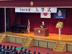 体育館で行われた入学式の壇上で新校長が式辞を述べている様子の写真