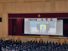 体育館で行われた入学式の壇上でプロジェクターを使い生徒会執行部からのメッセージを届ける様子の写真