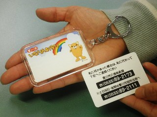 右手の手のひらの上に、「豊川市いなりんお守り」と黄色のマスコットキャラクターが記載されているキーホルダーと、左手に緊急連絡先と登録番号が書かれたカードを持っている人の写真
