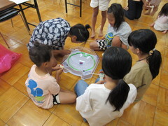 床に置かれたコマを回す台を中心に5名の子どもが輪になって座っている写真