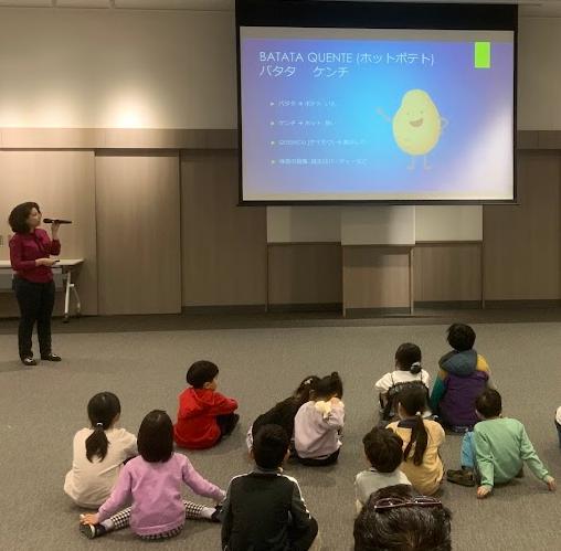 赤色の服を着たブラジル人女性がスクリーンの前で話をしている写真