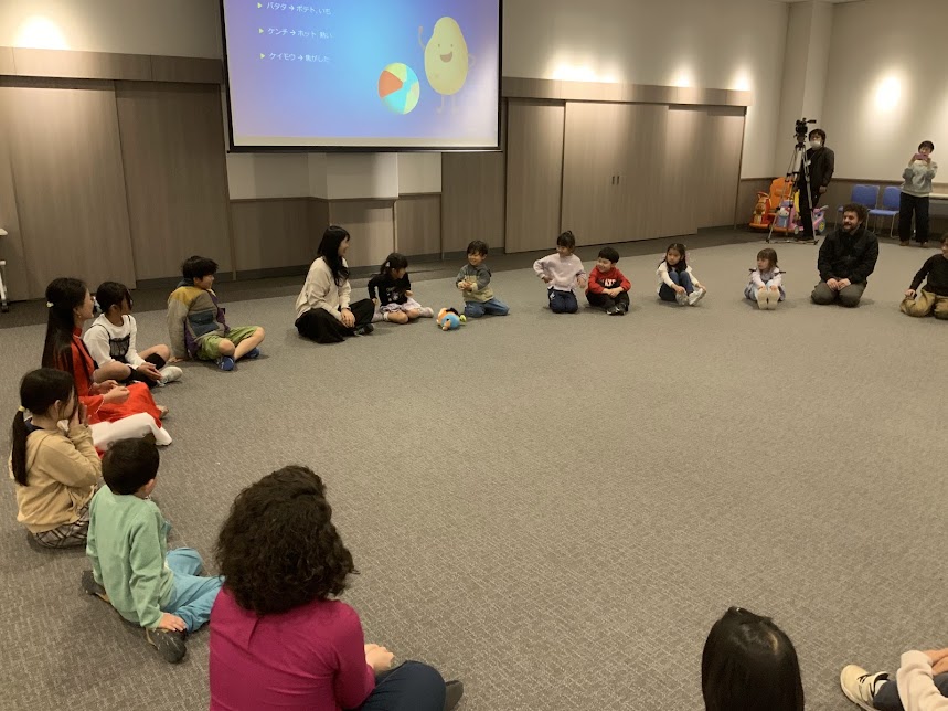 親子がスクリーンの前に円になって座っている写真