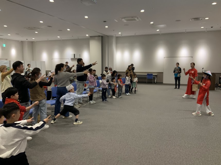 赤色のベトナムの服を着た女の子と参加者がじゃんけんをしている写真