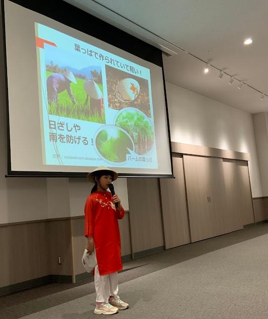 赤色のベトナムの服を着た女の子がパワーポイントを使いながら話をしている写真