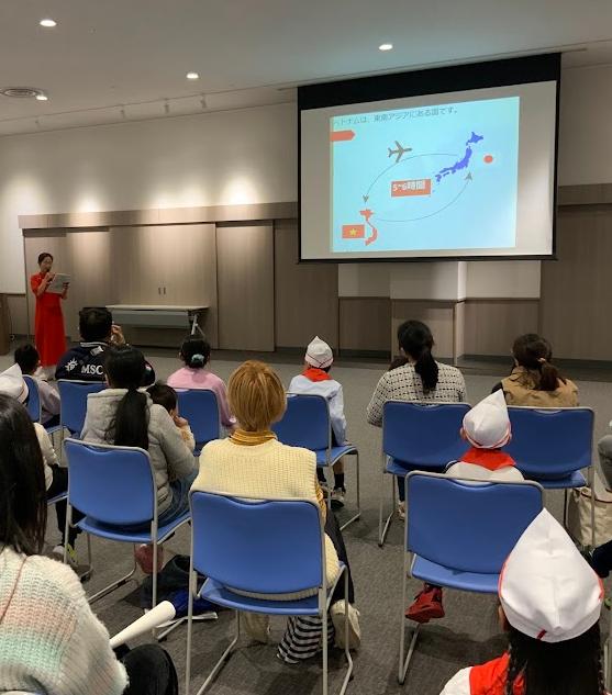 赤色のベトナムの服を着た女性がパワーポイントを使いながら話をしている写真