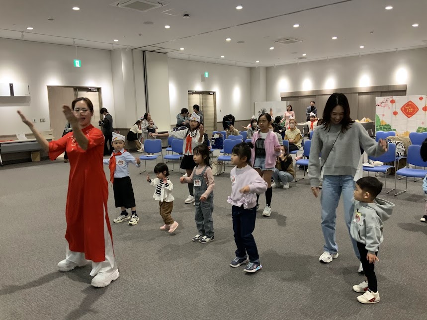 赤色のベトナムの服を着た女性が子供たちにダンスを教えている写真