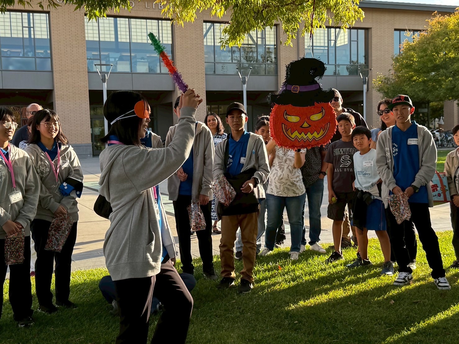 灰色のポーカーを着た女子中学生がアイマスクをして吊るしてあるカボチャのおもちゃをたたこうとしているところを、多くの中学生が見ている写真