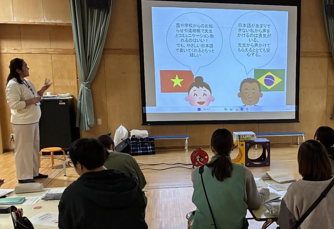 女性パワーポイントを見せながら複数の保育士に説明している写真