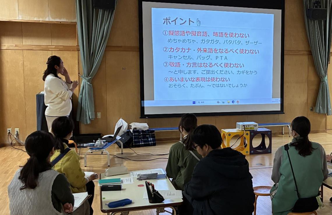 女性パワーポイントを見せながら複数の保育士に説明している写真