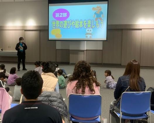 水色の服を着た男性がスクリーンの前で話をしている写真