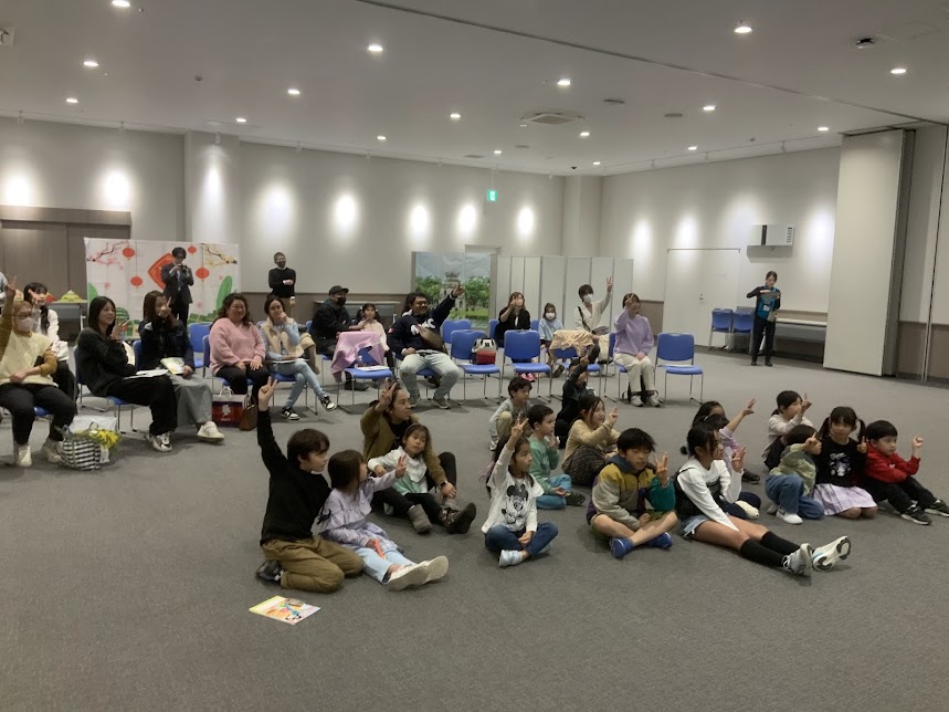 会場で座っている親子が手を挙げている写真