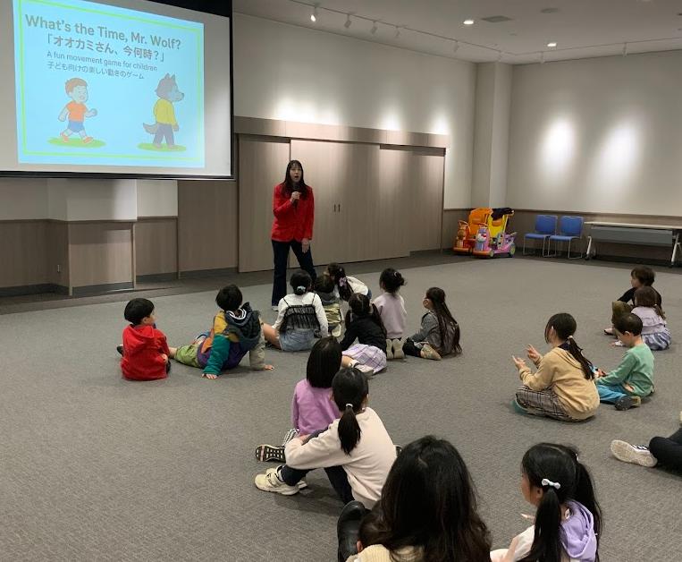 赤色の服を着たオーストラリア人女性がスクリーンの前で話をしている写真