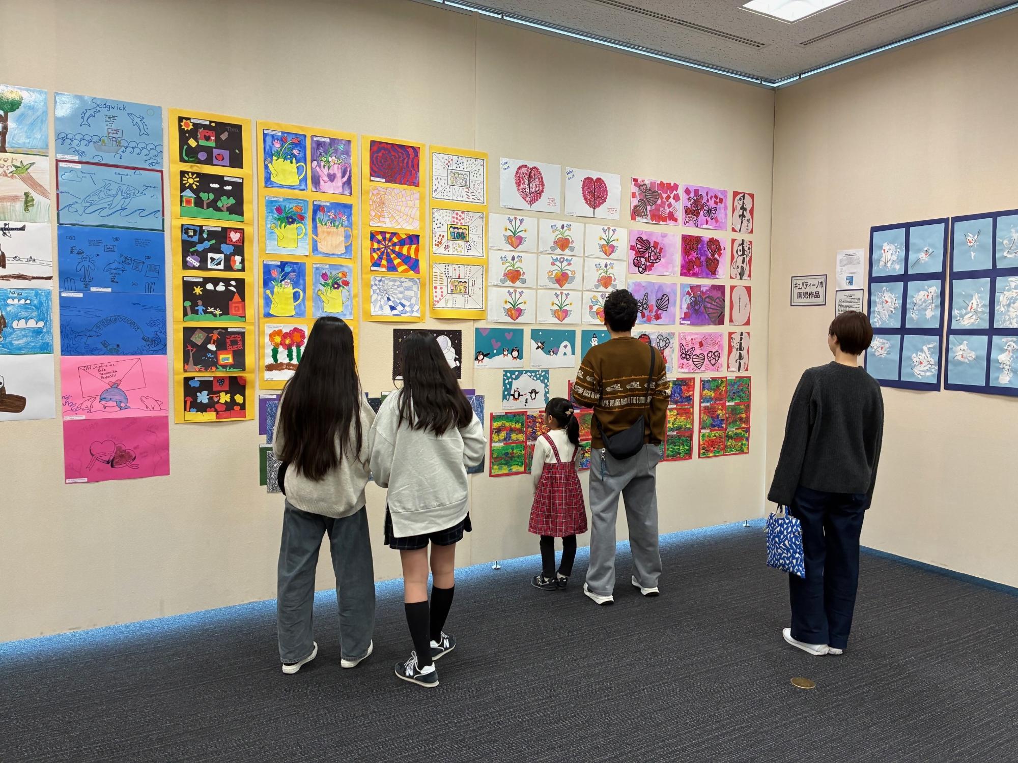 父、母、3人の娘がキュパティーノ市の子どもたちが描いた絵を見ている写真