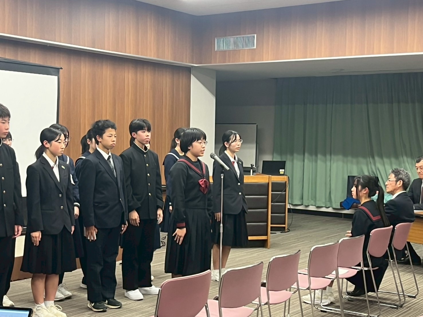 制服を着た女子生徒がスタンドマイクを使って発表している写真