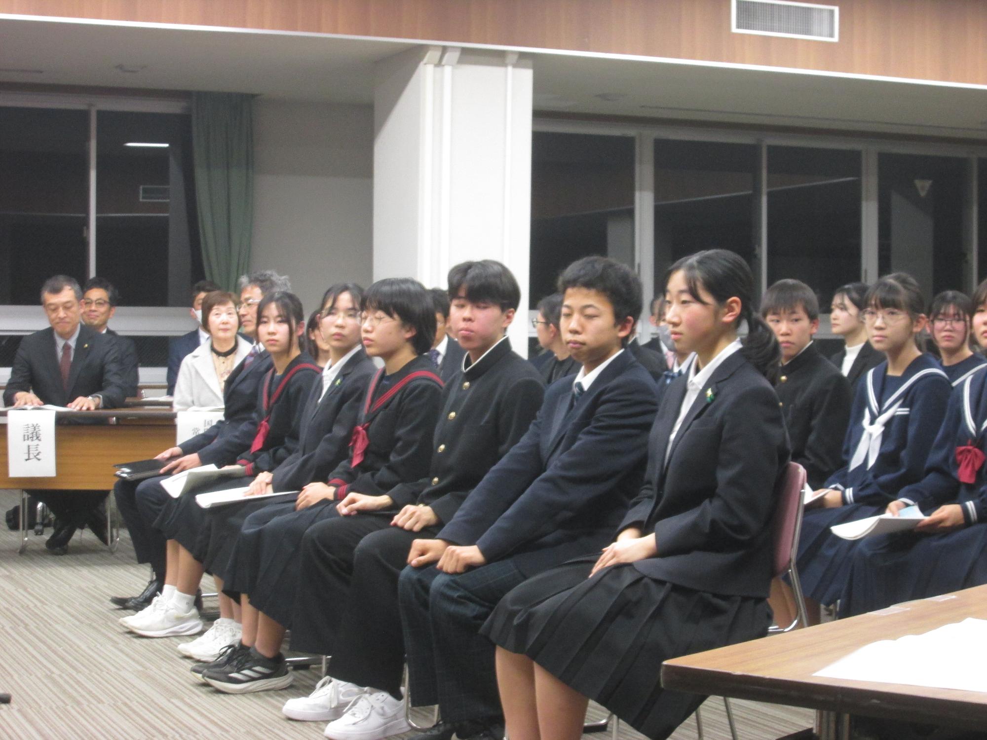 制服を着た複数の中学生が椅子に座っている写真