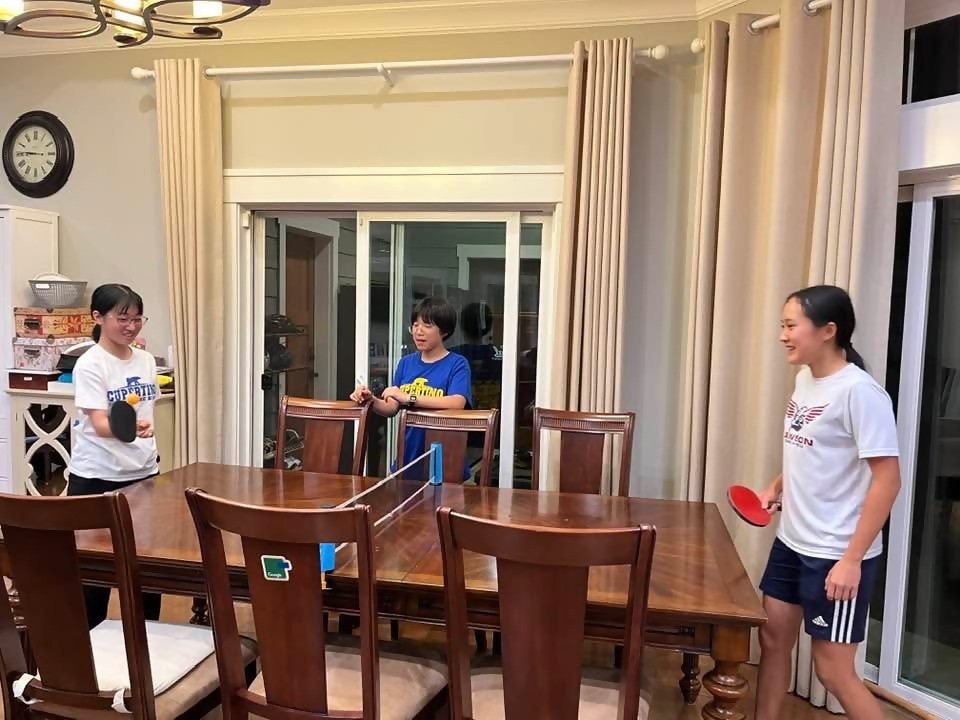 白い服を着た女の子2人が卓球をしているところを青い服を着ている女の子が見ている写真