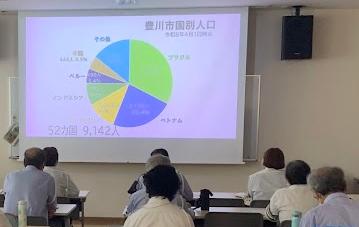 女性パワーポイントを見せながら複数の交通指導員に説明している写真