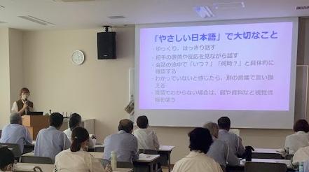 女性がパワーポイントを見せながら複数の交通指導員に説明している写真