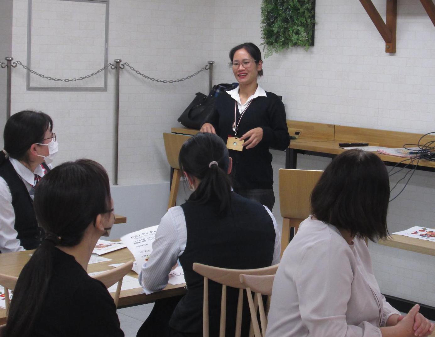 スーツを着た女性が、座っている銀行員の女性たちの前で説明している写真