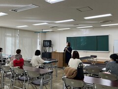 教室の演台横で話す人を席についてみている人たちの写真