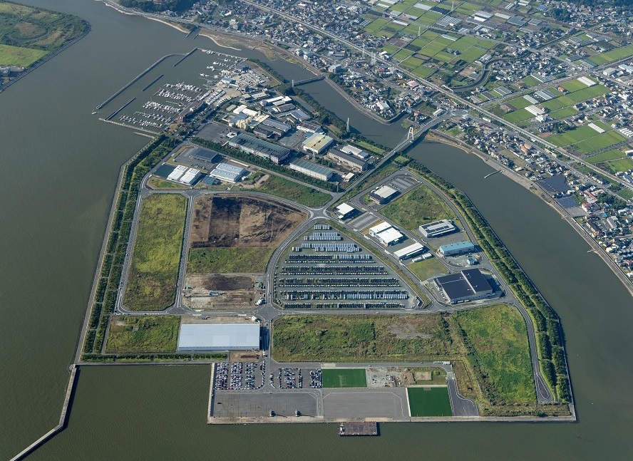 海に面した緑の平地の一画に、多くの大きな建物が立ち並んでいる様子をメインとして、辺り一面を空から写した航空写真