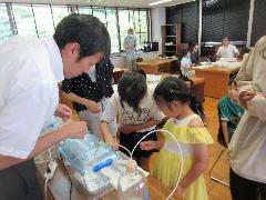 3人の子どもたちが目の前の長テーブルに置かれている実験の装置や印刷された用紙を見ている写真