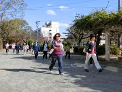 青空の下で公園内の道を歩いているウォーキング教室参加者の人たちの写真