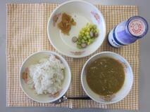 テーブルクロスに並べられた麦ごはん・牛乳・米粉のカレーライス・えだ豆とコーンのソテー・福神漬の写真