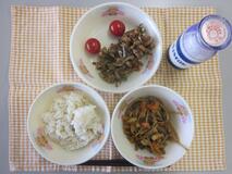 テーブルクロスに並べられた玄米ごはん・牛乳・細切りやさいの炒め煮・大豆と小魚のごまがらめ・ミニトマトの写真