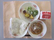 テーブルクロスに並べられた白玉うどん・牛乳・きつねうどん・大学いも・しんこあえの写真