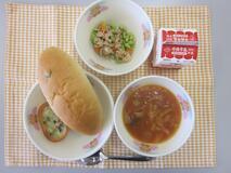 テーブルクロスに並べられたレーズンロールパン・牛乳・ミネストローネ・やさいグラタン・ツナとえだ豆のソテーの写真