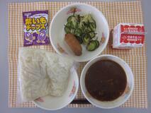 テーブルクロスに並べられた白玉うどん・牛乳・みそ煮込みうどん・いなりずし・きゅうりの塩こんぶあえ・さつまいもチップスの写真