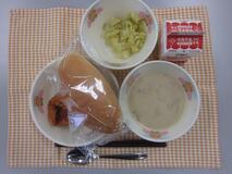 テーブルクロスに並べられた愛知の米粉入りパン・牛乳・豆乳スープ・揚げどり肉のトマトソースかけ・キャベツソテーの写真