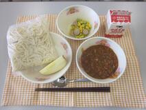 テーブルクロスに並べられたソフトめん・牛乳・ミートソース・えだ豆とコーンのソテー・りんごの写真
