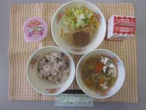 テーブルクロスに並べられた赤はん・牛乳・ゆずのすいもの・チキンハムカツ・ボイルキャベツ・お祝いいちごゼリーの写真