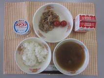 テーブルクロスに並べられたごはん・牛乳・のっぺい汁・ぶた肉のしょうが炒め・ミニトマト・ヨーグルトの写真