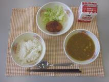 テーブルクロスに並べられたごはん・牛乳・米粉のカレースープ・メンチカツ・ボイルキャベツの写真