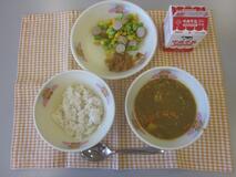 テーブルクロスに並べられた麦ごはん・牛乳・米粉のカレーライス・えだ豆とコーンのソテー・福神漬の写真