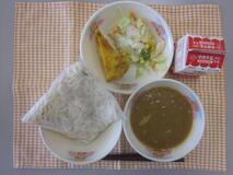 テーブルクロスに並べられたソフトめん・牛乳・米粉のカレーソース・スパニッシュオムレツ・コールスローサラダの写真