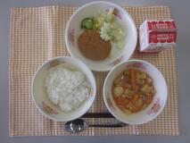 テーブルクロスに並べられたごはん・牛乳・とり肉とやさいのケチャップ炒め煮・コロッケ・コーンサラダの写真