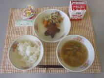 テーブルクロスに並べられたごはん・牛乳・きらきらすまし・ほし型ハンバーグ・三色炒め・たなばたゼリーの写真