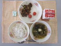 テーブルクロスに並べられた麦ごはん・牛乳・わかめスープ・ビビンバ・ミニトマト・角チーズの写真