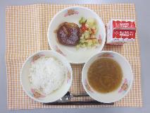テーブルクロスに並べられたごはん・牛乳・やさいスープ・とうふハンバーグのワインソースかけ・カラフルソテーの写真