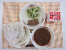 テーブルクロスに並べられた白玉うどん・牛乳・みそ煮込みうどん・いなりずし・青菜あえの写真