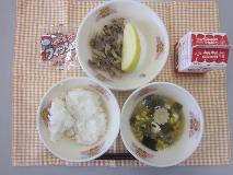 テーブルクロスに並べられたごはん・牛乳・中華スープ・ぶた肉のオイスターソース炒め・りんご・アーモンド小魚の写真