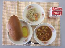 テーブルクロスに並べられたくろロールパン・牛乳・ミートボールのトマト煮・コーングラタン・ツナとやさいのソテーの写真