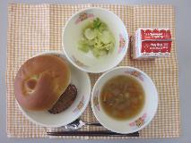 テーブルクロスに並べられたサンドイッチバンズパン・牛乳・コンソメスープ・てりやきハンバーガー（てりやきハンバーグ/キャベツソテー）の写真
